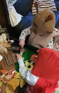 Two children in costumes, playing with owl and caterpillar toys and books 