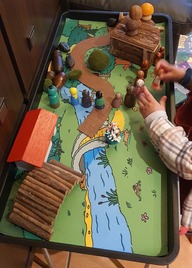 Two young children's hands, playing with some small plastic figures in a tray