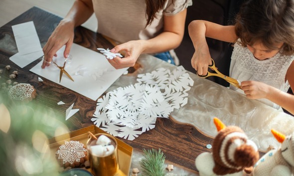 Aerial view of an adult and child making snowflakes out of paper at a Christmassy-decorated table