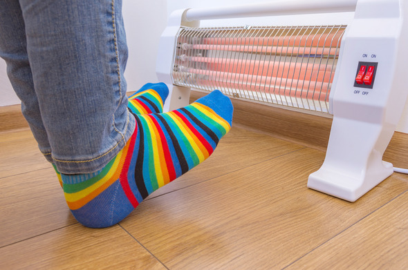 A person in colourful stripy socks heating their feet on an electric heater