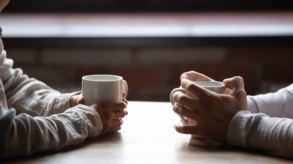 Two people's hands holding hot drinks sat inside at a table