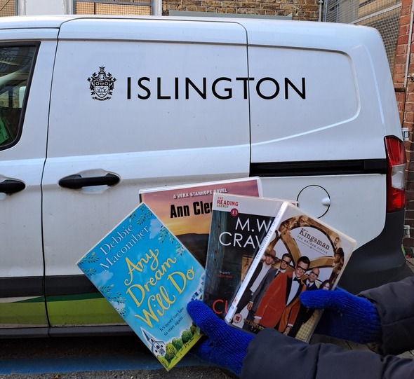A person in blue gloves holding a selection of books in front of an Islington Council branded white van