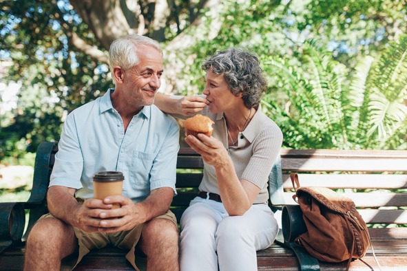 A lovely elderly couple sat outside on a park bench enjoying the sun together