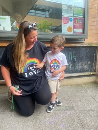 A woman crouched down with a small boy. Both are wearing a t shirt which reads 'Love is love'