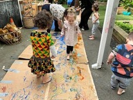 Young children using their bare feet to paint on a large flattened cardboard box