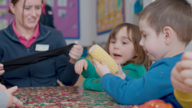 Two young children and an adult looking at a corn on the cob