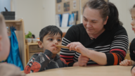 A young child with some food in his mouth. Sitting next to him is an adult.