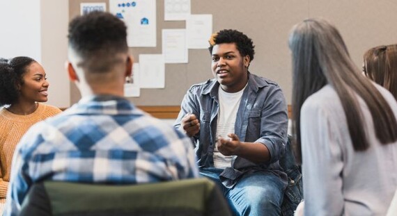 Young people sit in circle holding a discussion