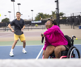 A black woman in a wheelchair enjoys a game of tennis