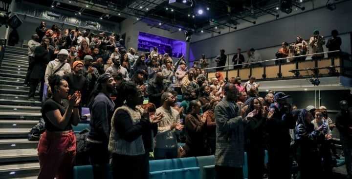 Gathering of young people from Poetic Unity clapping on stands facing a stage