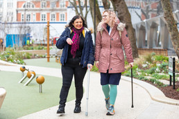 Two women with walking sticks stroll through the park
