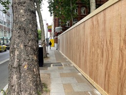 Wooden hoarding runs along the street leaving space on the pavement for people to walk past