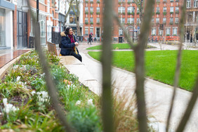 Image of a woman with a walking stick sat on the long benches among planting enjoying looking at the park