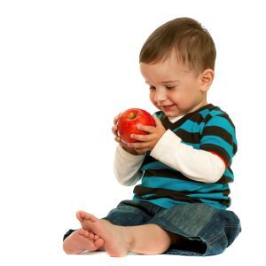 A young toddler looking at an apple and smiling