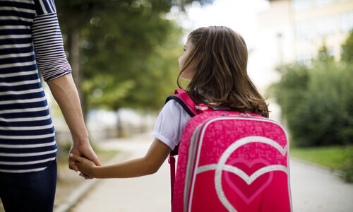 Young girl wearing a rucksack holding a parent's hand