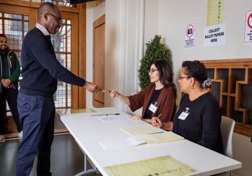 A person handing a ballot paper to someone in an office