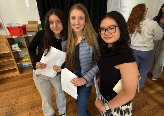 Three local girls posing with their GCSE result papers at school