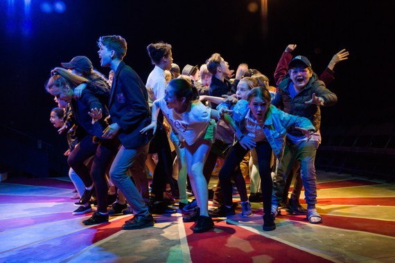 Young people huddled in a group in the centre of the image - in the midst of a theatrical performance