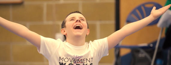 boy wearing movementworks t-shirt grinning and holding his arms in the air