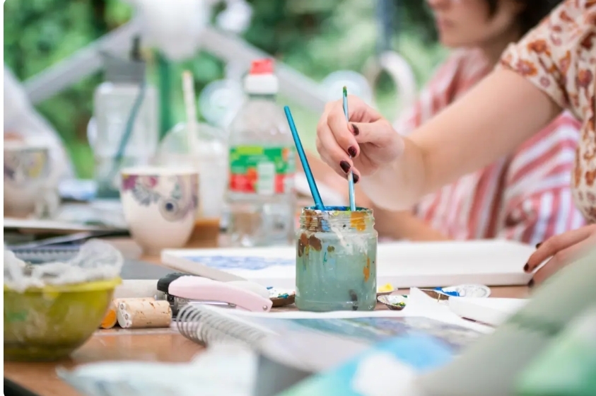 A Hand Dips Paintbrushes Into Water