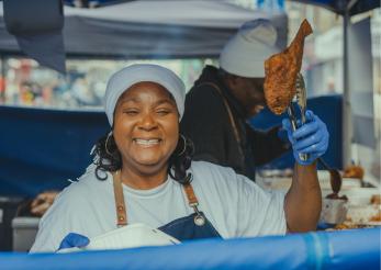 Chef smiling at the camera holding a large cooked chicken leg