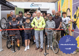 Carneys Bike Shop - Picture of opening day, group of people with bikes and person cutting ribbon