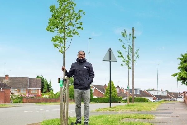 A photo of a man standing next to a semi-mature street tree he has sponsored