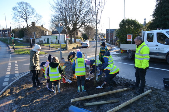 Image shows children from Featherbank Primary School in hi-vis jackets helping to plant trees