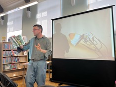 A man delivering a talk in front of a screen with a presentation