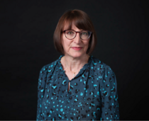 An image of a middle aged white woman in a blue patterned shirt facing the camera 