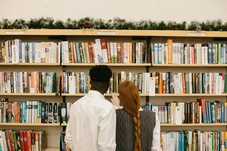 Two people browsing bookshelves with a festive wreath across the top