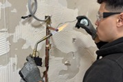Person working on a gas pipe with a blow torch