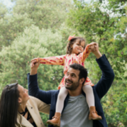 A family stood together. The child is on the dads shoulders.