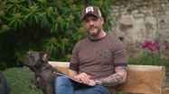 Tom Hardy sitting on bench outside with a book and french bulldog