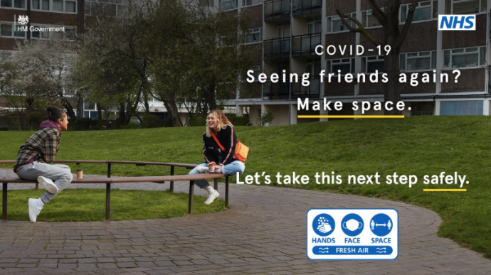 TEXT: COVID-19. Seeing friends again? Make space. Let's take this next step safely. PHOTOGRAPH: two friends sat on a bench outside residential flats