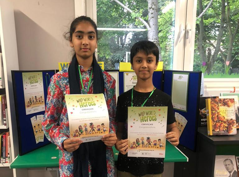 Two children in a library holding a certificate from the summer reading challenge.