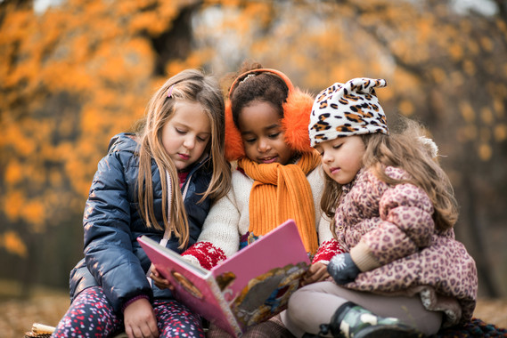 Three children reading a book in a park