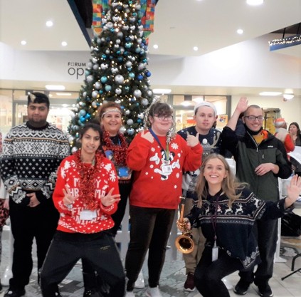 smiling people in Christmas jumpers in front of a big Christmas tree