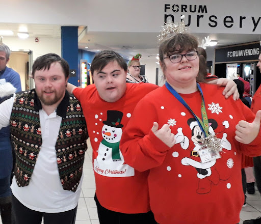 3 pale-skinned young people with Christmas jumpers on. They are hugging each other