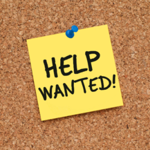Help wanted written on a yellow post-it note pinned onto a cork board