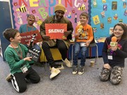 Lemn Sissay laughing with a group of young children in a library