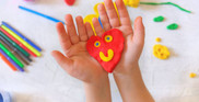 A photo of a child's hands holding a heart made from plasticine