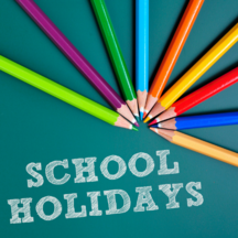 A range of pencil crayons on a green background with text 'school holidays'