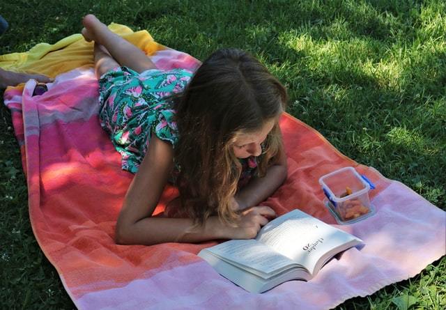Child lying on blanket in garden reading a book.