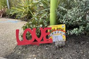 'Find My Happy' book by Emily Coxhead next to a sculpture of the word love in a garden