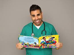 Dr Ranj in scrubs with stethoscope around his neck, reading his book 'A Superpower Like Mine@