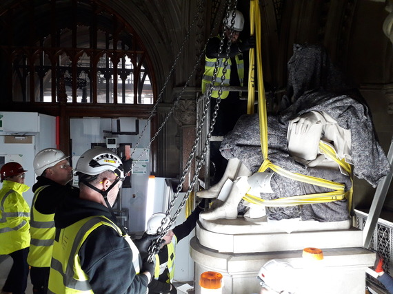 Image shows workers in hi-vis jackets checking a strap that's holding one of the statues.