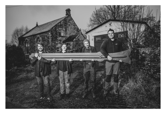 Image shows members of the team at Cumbria Clocks outside the workshop. They are holding a ten-foot long minute hand from the Town Hall clock.