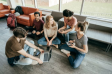 A group of people sat round talking with laptops and phones 