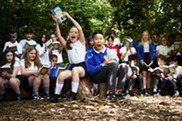Year 6 class of primary school children, sat in a clearing, holding books up.